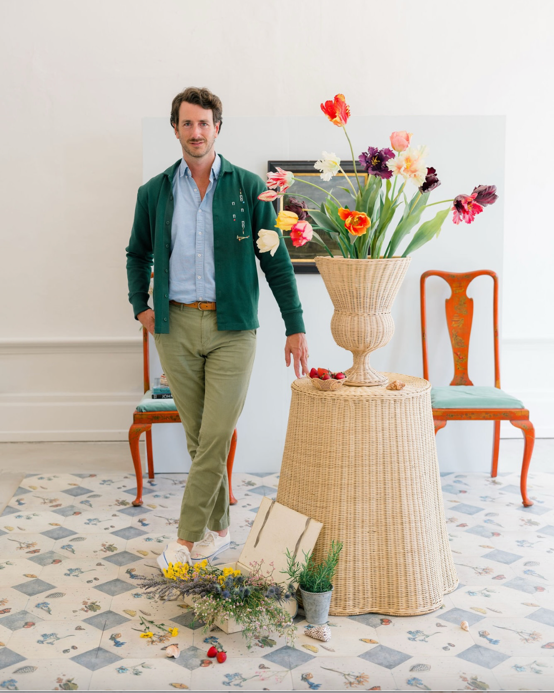 Man standing next to a table with a large vase of flowers in a room with chairs and decor.